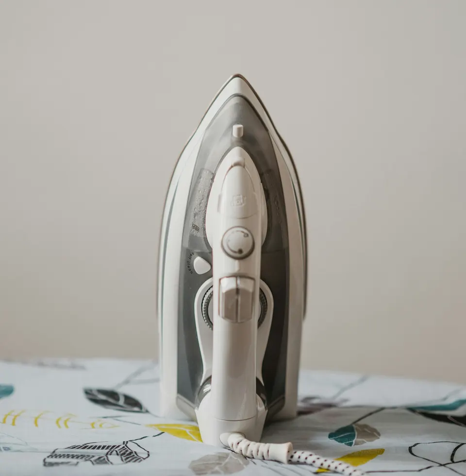 White steam iron standing upright on an ironing board