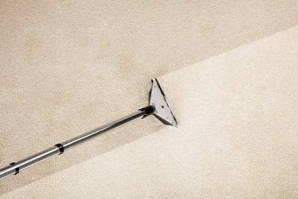 Extraction wand lifting dirt from a cream carpet